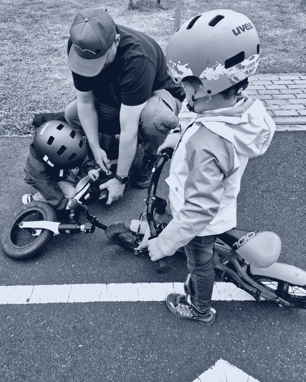 Der Gründer, in der Hocke am Lenker eines Laufrads, dabei zwei Kinder mit Fahrradhelmen auf einem Verkehrsübungsplatz